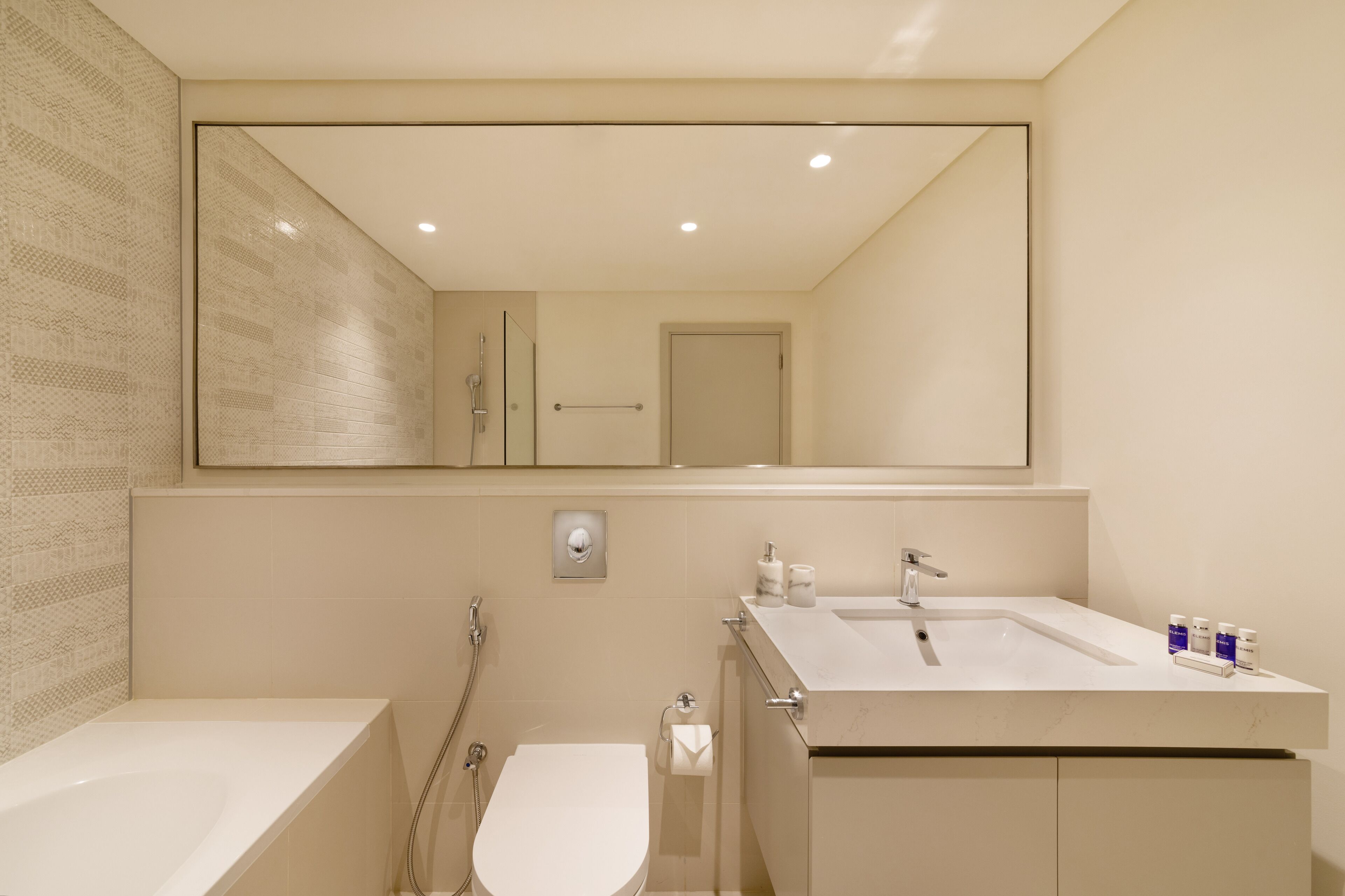 Un bagno moderno con uno specchio grande, una vasca, un water e un lavandino con articoli da toilette.