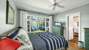 A bedroom with a bed, a TV, a ceiling fan, and a view of the outdoors. - 4 Bedroom Waterfront Home With Beatutiful Lake and Mountain Views (Moultonborough)
