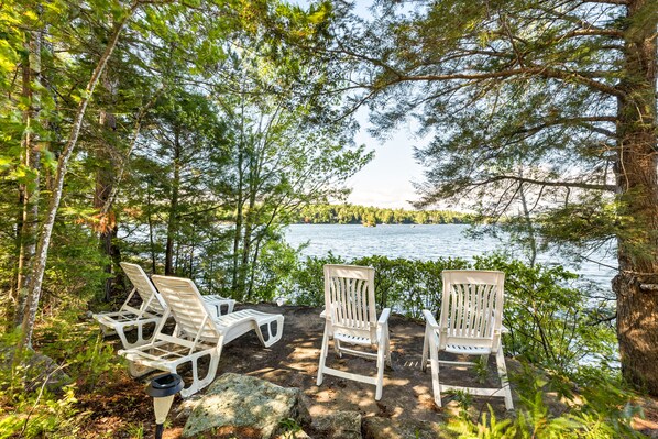 Three white Adirondack chairs by a lakeside with a forest backdrop. - Knotty and Nice Winnipesaukee Waterfront Cottage Sleeps 6 (Moultonborough)