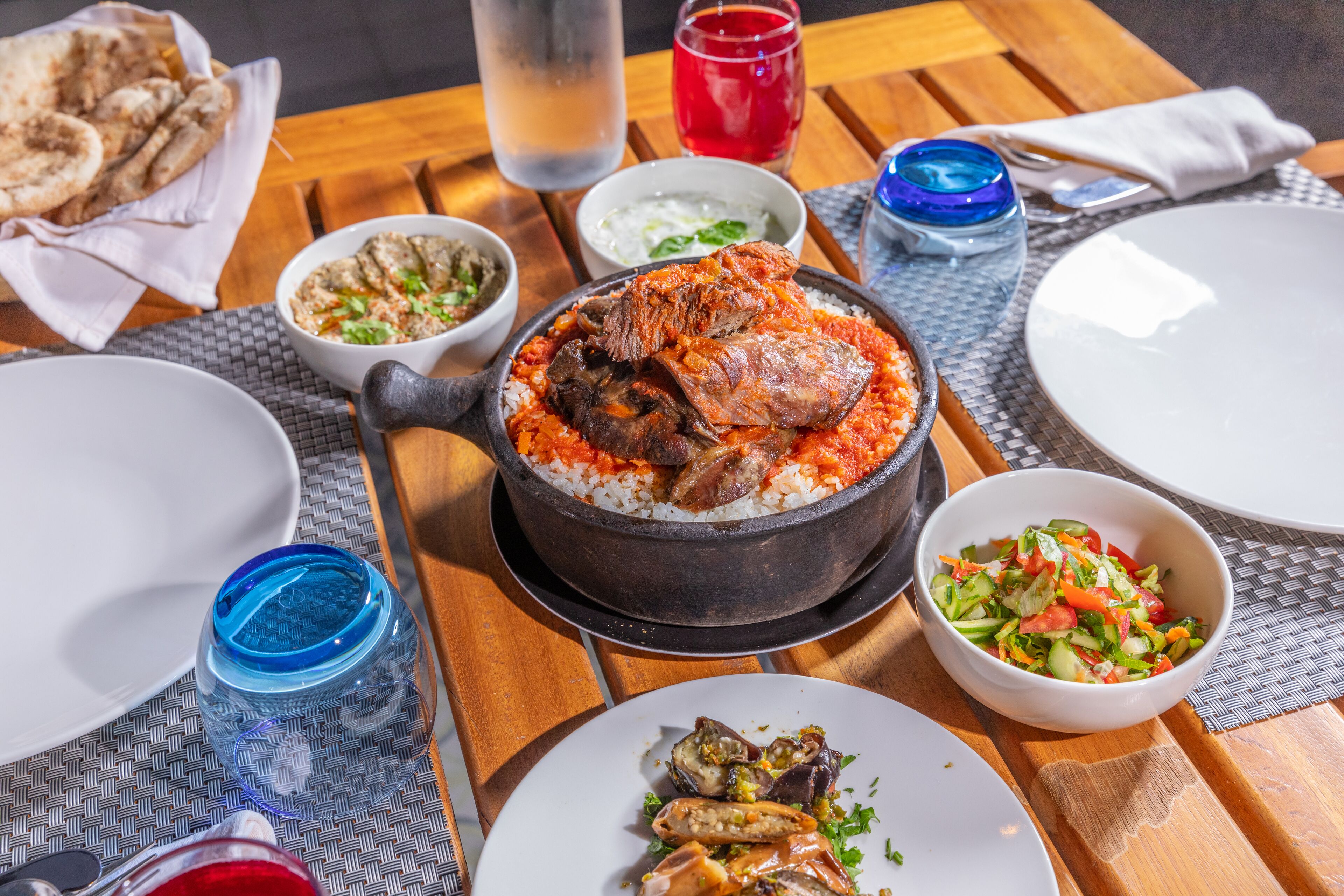 A dining table with a variety of dishes including a pot of rice with meat, a bowl of salad, and several glasses of beverages.