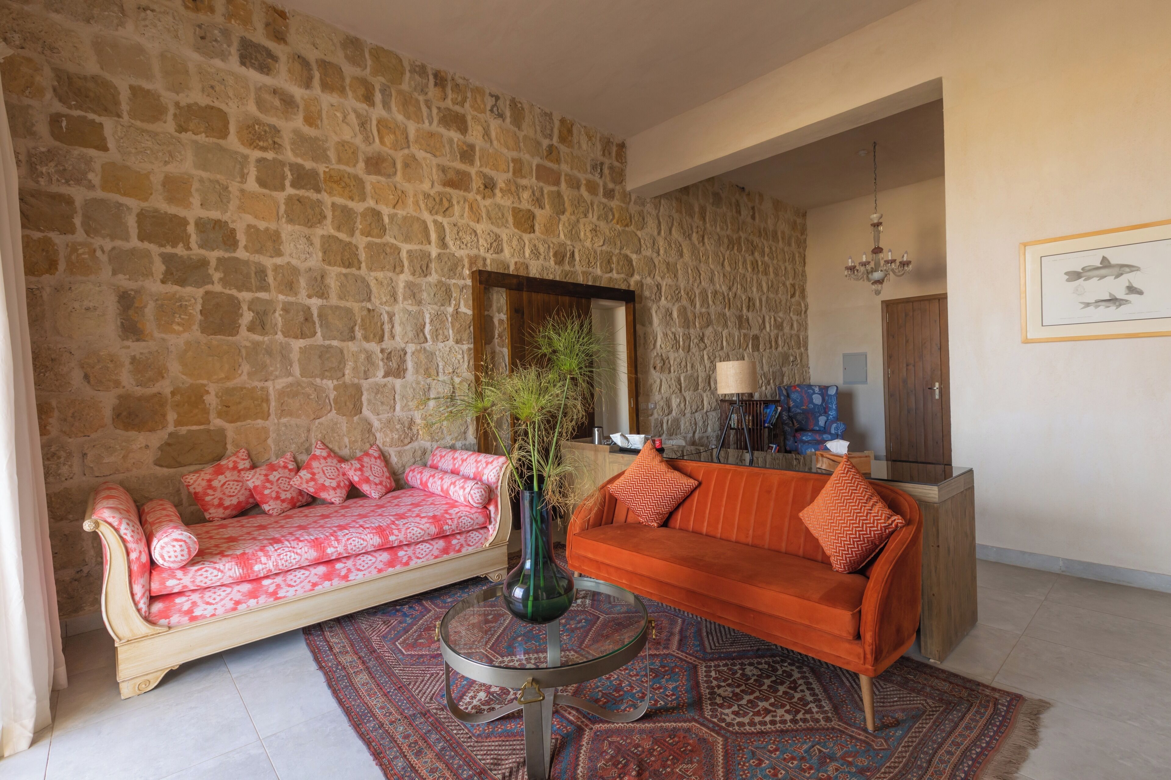 A living room with a stone wall, a red sofa, a pink sofa, a glass coffee table, and a patterned rug.