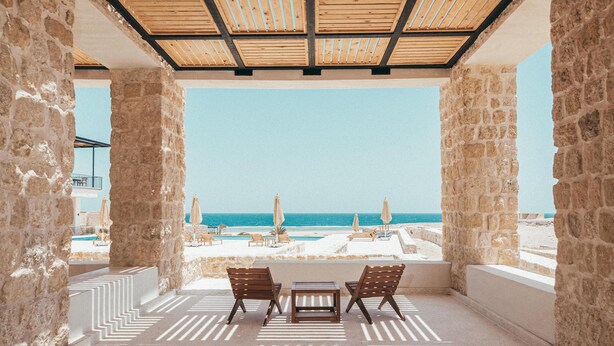 A covered outdoor seating area with stone walls, a view of the beach, and umbrellas. - Wadi Sabarah Lodge (Marsa Alam)