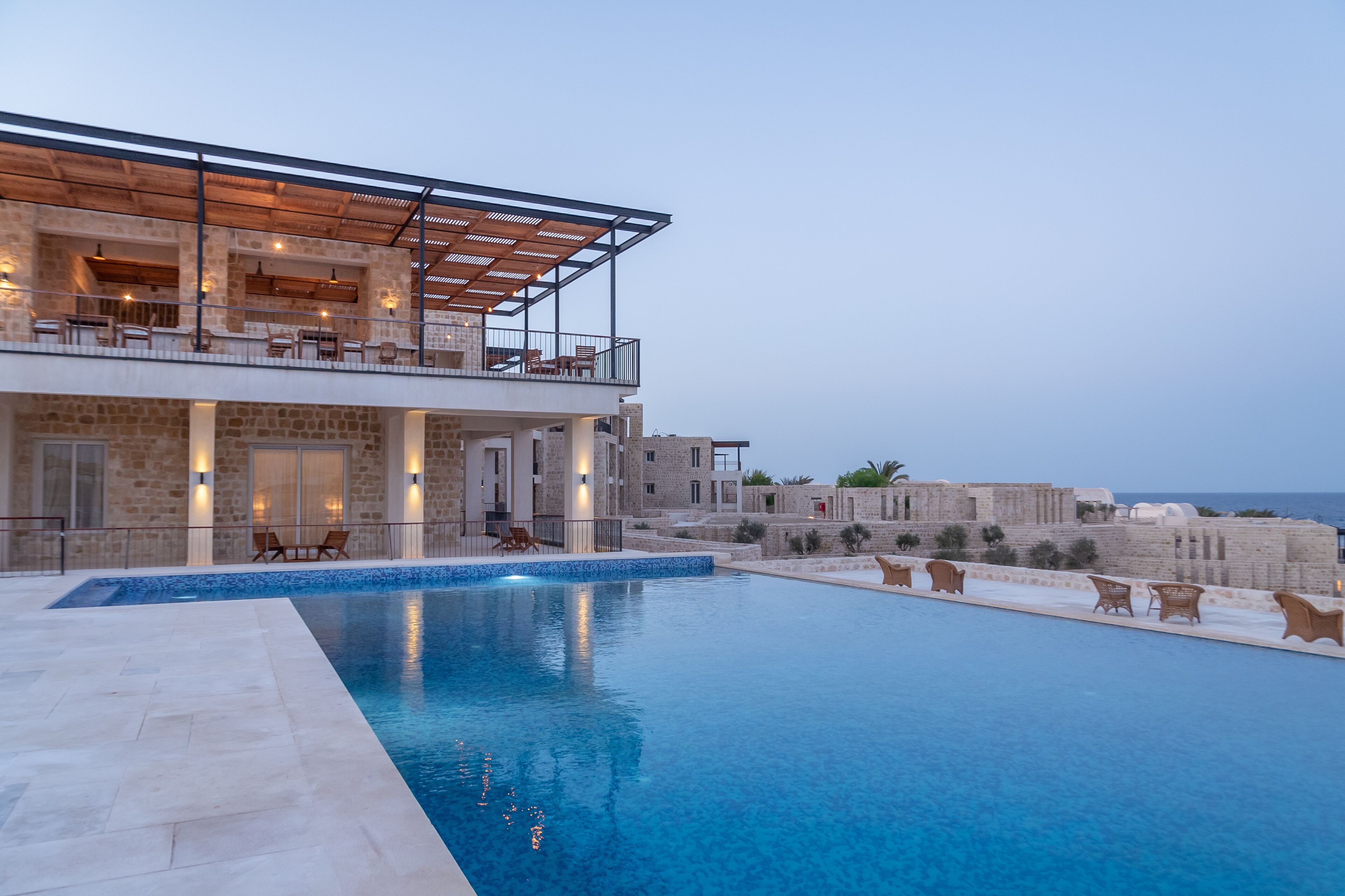 A modern building with a pool, outdoor seating, and stone walls.