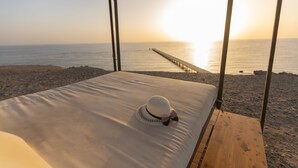 A bed with a hat on it, a wooden deck, and a view of the sea and a pier. - Wadi Sabarah Lodge (Marsa Alam)