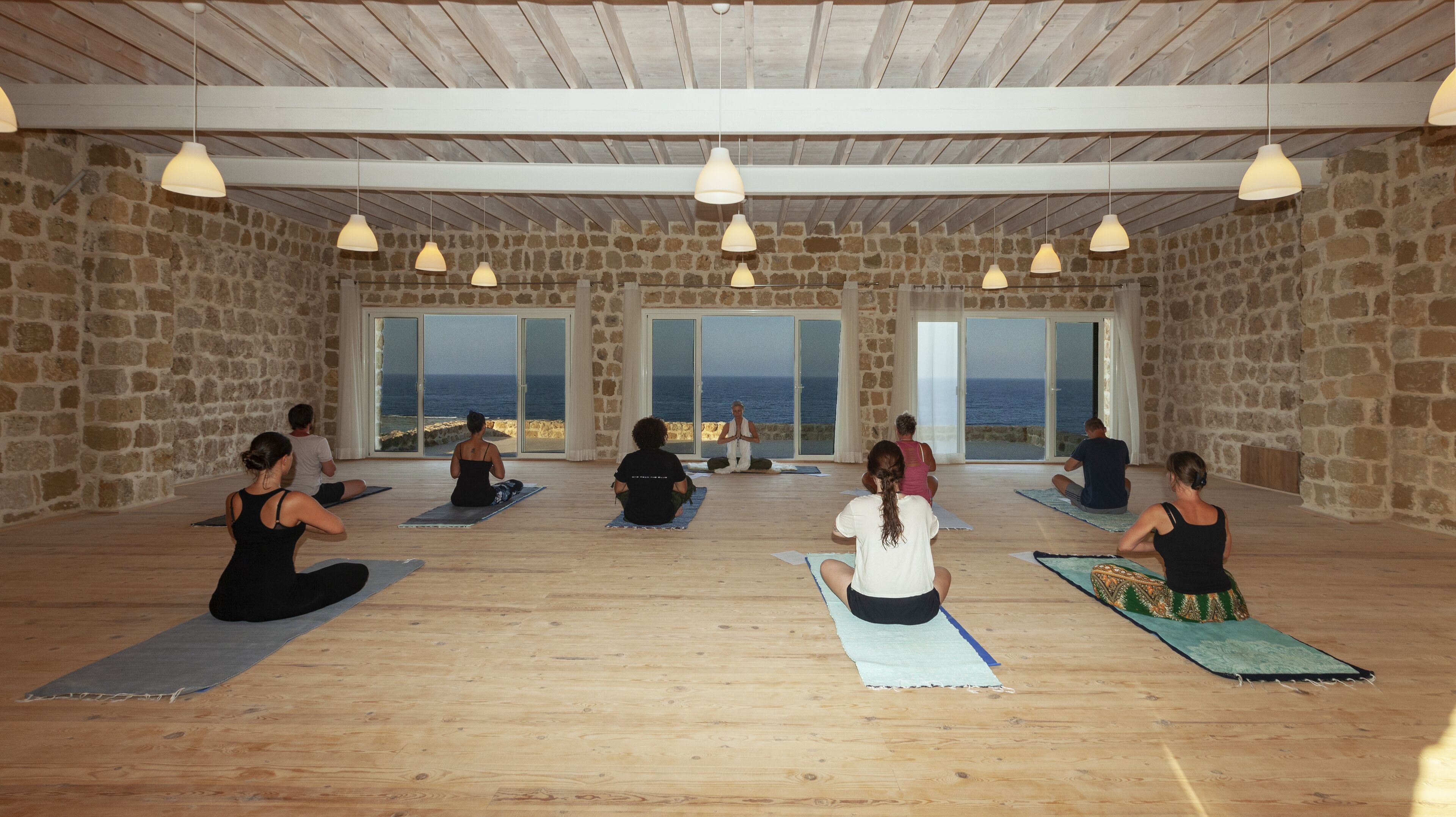 A yoga studio with stone walls, large windows, and wooden floors.
