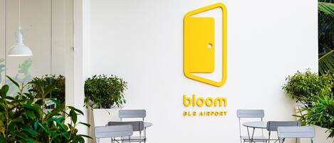 En væg med et logo og tekst, der viser "bloom BLA AIRPORT". Borde og stole er placeret i forgrunden.