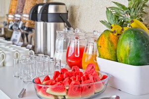A breakfast buffet with a variety of fruits, including watermelon and pineapple, and a coffee machine in the background.
