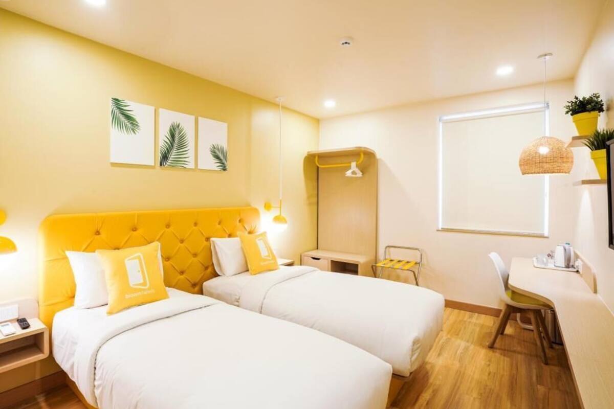 Una habitación de hotel con dos camas, una mesita, una silla, un espejo y una ventana.