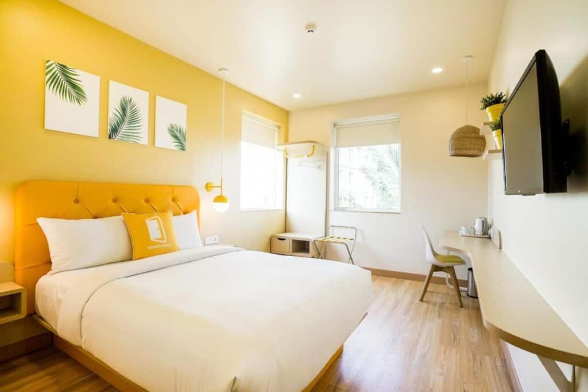 Una habitación de hotel con cama, escritorio, silla, televisión y obras de arte en la pared.