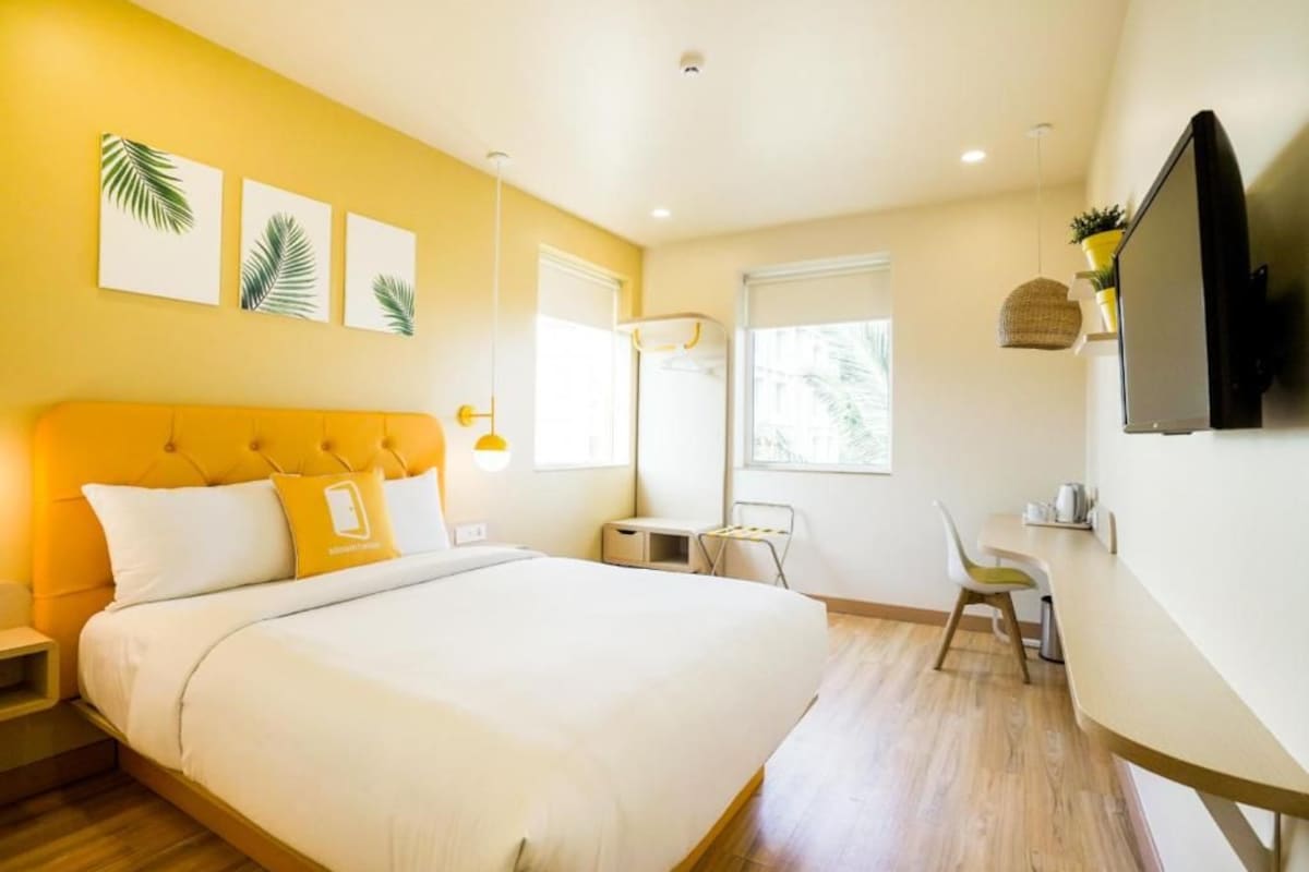 A hotel room with a bed, a desk, a chair, a television, and artwork on the wall.
