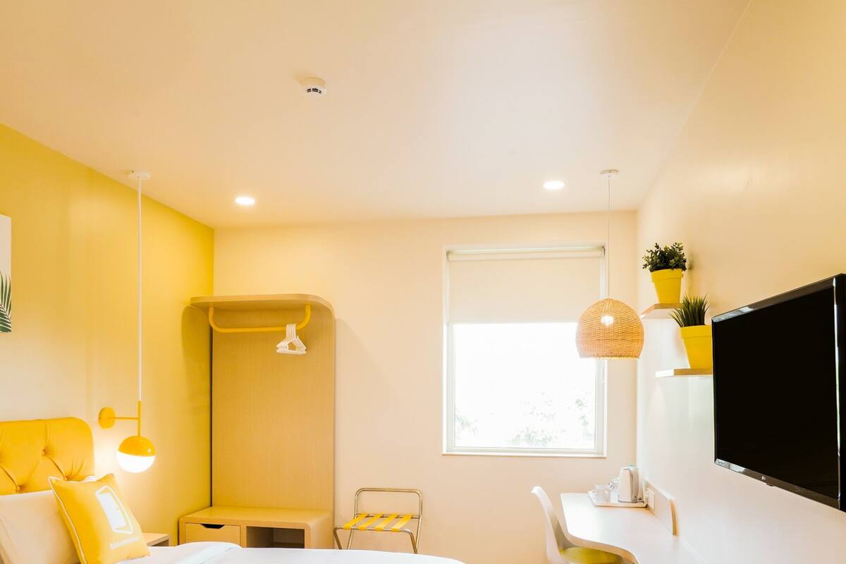 Una habitación de hotel moderna con dos camas, un escritorio, una silla, un televisor y una ventana.