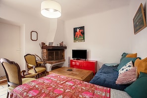 A room with a bed, a sofa, a television, a fireplace, and a poster on the wall.