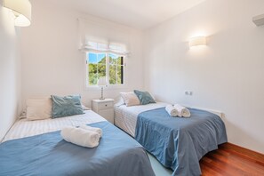 Un dormitorio con dos camas, una ventana con cortinas, lámparas de noche y una mesita de noche.