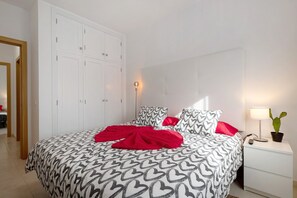 Un dormitorio con cama, armario blanco, lámpara de noche y planta en maceta.