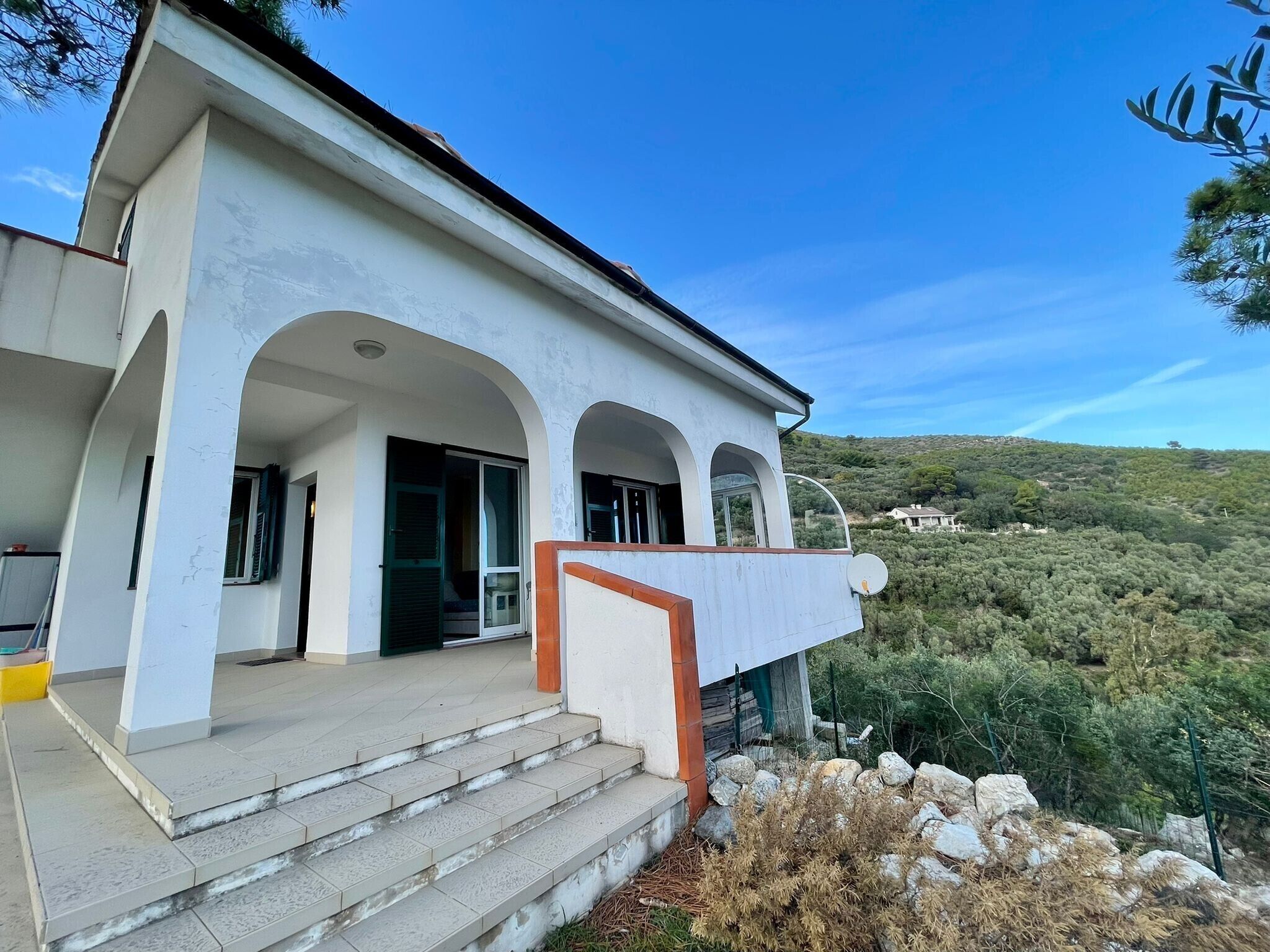 Ein modernes Gebäude mit heller Fassade, einem Rundbogen-Eingang und einem Balkon mit Blick auf eine hügelige Landschaft.