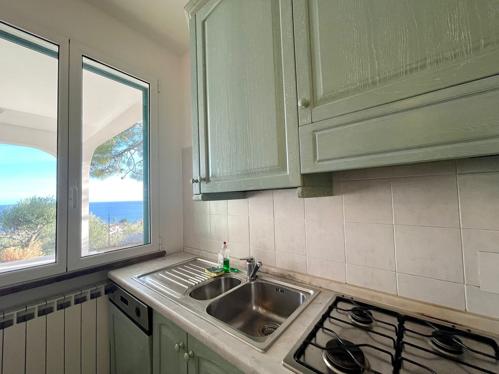 A kitchen with a window, a sink, a stove, and light green cabinets.