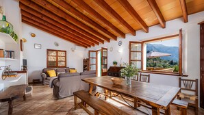 A spacious living area with a wooden ceiling, a large dining table, and a view of mountains through a large window. - Holiday Home 'Can Bordoy' with Mountain View, Pool, Garden & Terrace (FORNALUTX)
