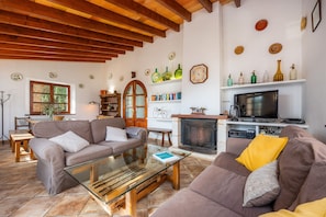 A living room with a fireplace, wooden beams, a television, and a bookshelf.