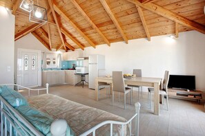 A room with a bed, a dining table with chairs, a TV, and a kitchen area with cabinets and a refrigerator.