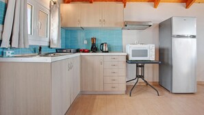 Una cocina con armarios de madera, microondas, refrigerador y una mesa con hervidor.