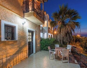 Un edificio de piedra con un balcón, una mesa con sillas y una palmera.