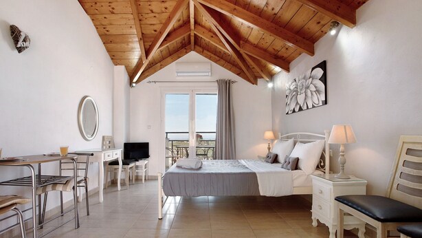 Una camera da letto con un letto, comodini, una scrivania, sedie, una televisione e un balcone con vista.