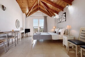 A bedroom with a bed, bedside tables, a desk, chairs, a TV, and a balcony with a view.