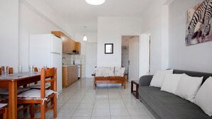 A living room with a sofa, a dining table with chairs, a kitchen area, and a framed picture on the wall. - Holiday Apartment "Yiannis Superior Apartment" with Sea View, Wi-Fi & Garden (Zakynthos)