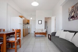 A living room with a sofa, a dining table with chairs, a kitchen area, and a framed picture on the wall.