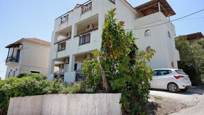 Un edificio residencial de varios pisos con balcones, un automóvil estacionado y un jardín.