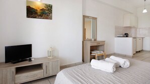 Una habitación de hotel con cama, televisión, escritorio con espejo, kitchenette y un cuadro en la pared.