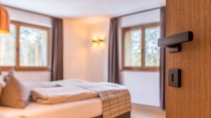 Une chambre à coucher avec un lit, des tables de chevet, une lampe fixée au mur et des fenêtres.