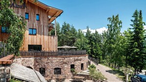 Un bâtiment en bois avec des murs en pierre, des places assises à l’extérieur et un escalier en pierre.