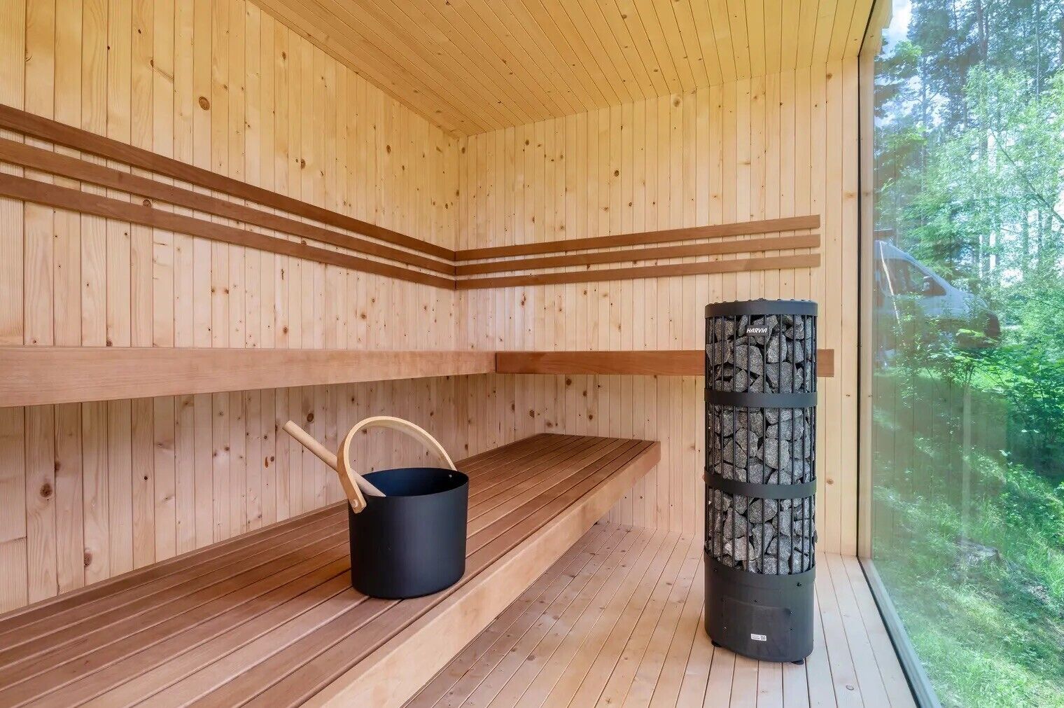 Un sauna avec des murs en bois et un banc, un appareil de chauffage de sauna noir, et une fenêtre donnant sur la forêt.
