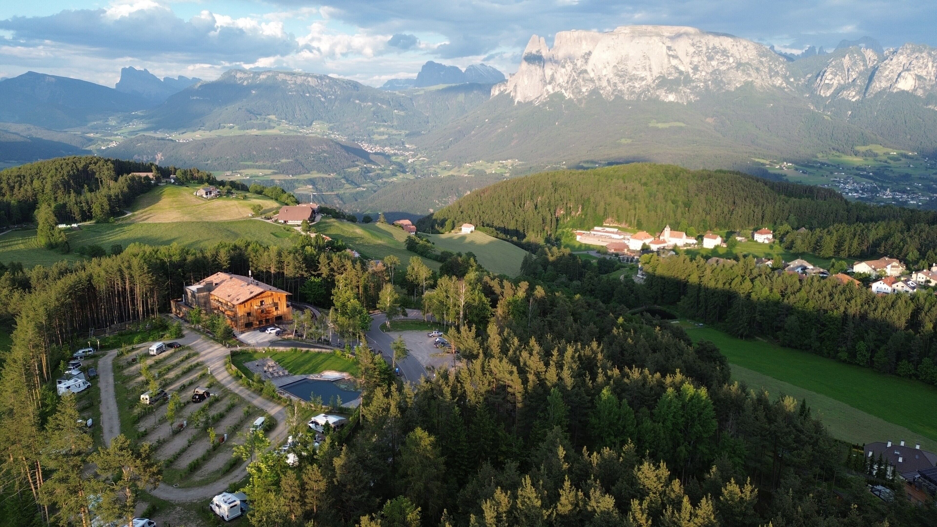 A mountainous landscape with a village, a large wooden building, and a pool.