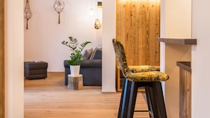 Un salon moderne avec un plancher en bois, un canapé gris, une petite table ronde agrémentée d’une plante et un tabouret de bar.