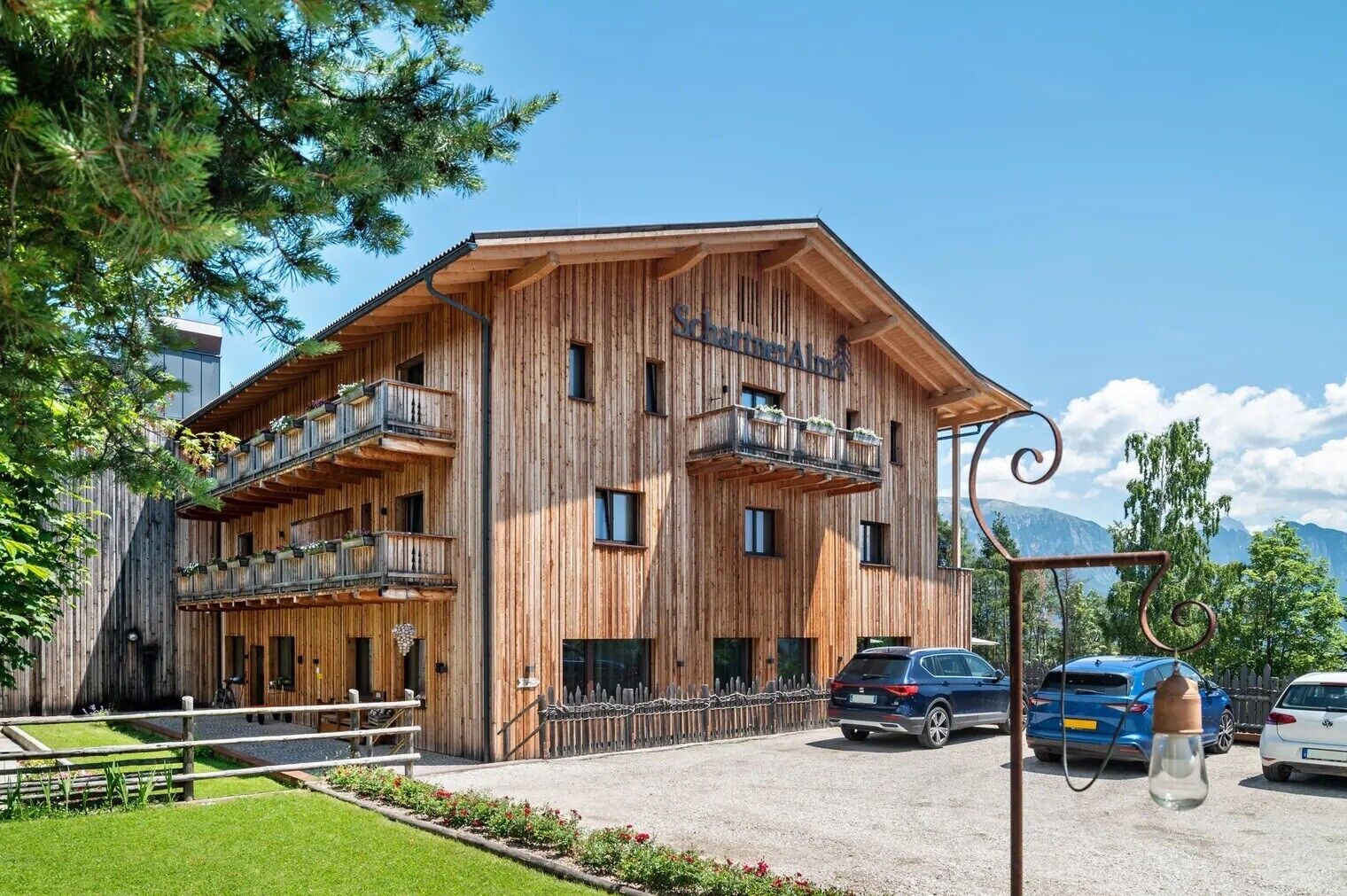 Un immeuble en bois à plusieurs étages, doté de balcons, d’un espace de stationnement et surplombant un paysage montagneux.