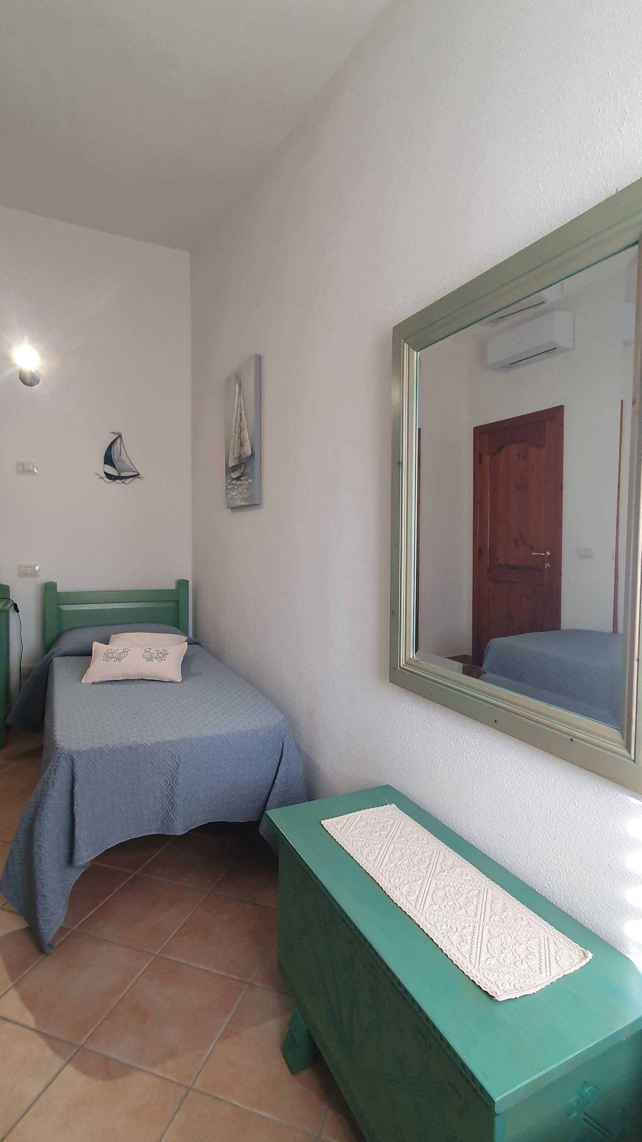 A bedroom with two beds, a green bedside table, a mirror, and a wall-mounted air conditioner.