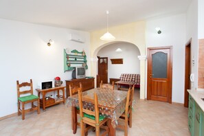 Uma sala de jantar com mesa de madeira, cadeiras, televisão e micro-ondas.