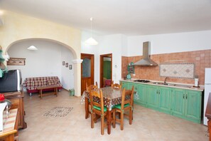 Uma sala de jantar com mesa e cadeiras, uma cozinha com armários verdes e um painel de azulejos.