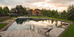 Une terrasse en bois avec une piscine, des chaises longues et un bâtiment en bois en arrière-plan.