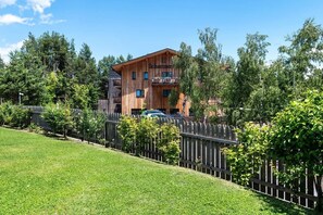 Un edificio in legno su più piani, con balconi, circondato da una recinzione in legno e vegetazione.