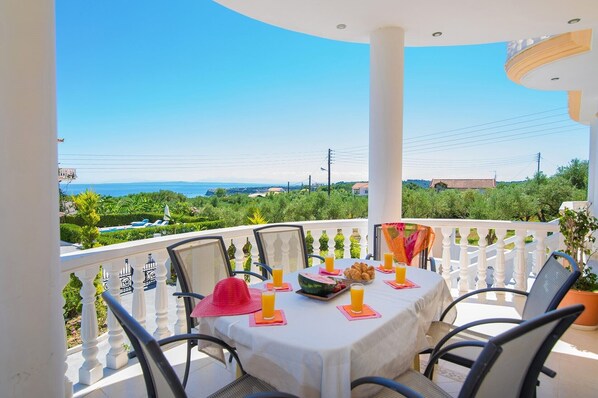 Une table dressée sur un balcon, avec vue sur la mer, entourée de chaises et recouverte d’une nappe.