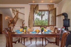 Comedor con mesa de madera dispuesta para el desayuno, una escalera y vista a espacios verdes al exterior.
