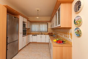 A modern kitchen with a stainless steel refrigerator, microwave, and oven, wooden cabinets, a tiled backsplash, and a fruit plate on the counter.
