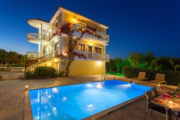 A multi-story hotel with a swimming pool, outdoor seating, and a well-lit balcony.