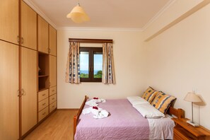 A bedroom with a bed, wooden wardrobe, window with curtains, and a lamp.