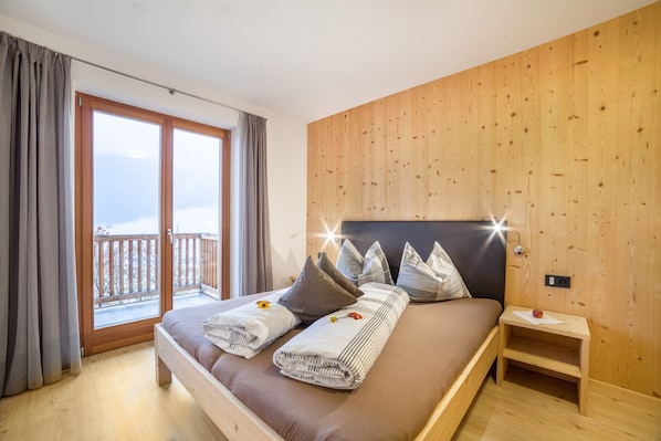A bedroom with a bed, pillows, a nightstand, a wooden wall, and a balcony.