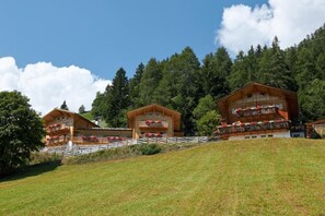 Une rangée de chalets en bois dotés de balcons, se dressant sur fond d’une forêt dense et d’un ciel dégagé.