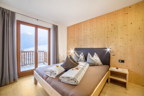 A bedroom with a bed, a nightstand, a wooden wall, and a balcony.